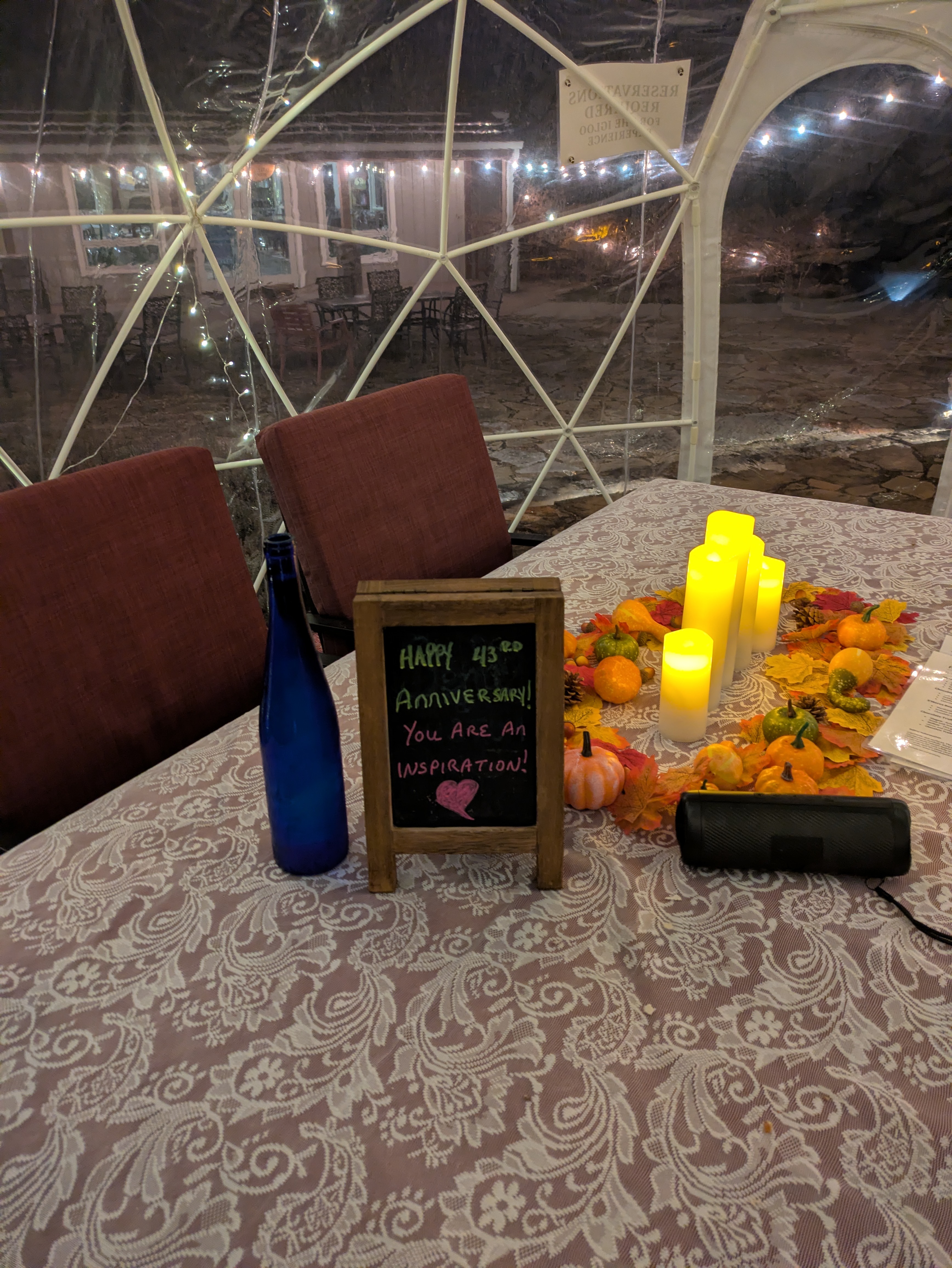 A candlelit table inside a Fence Stile igloo set with a handwritten anniversary chalkboard and autumn centerpiece