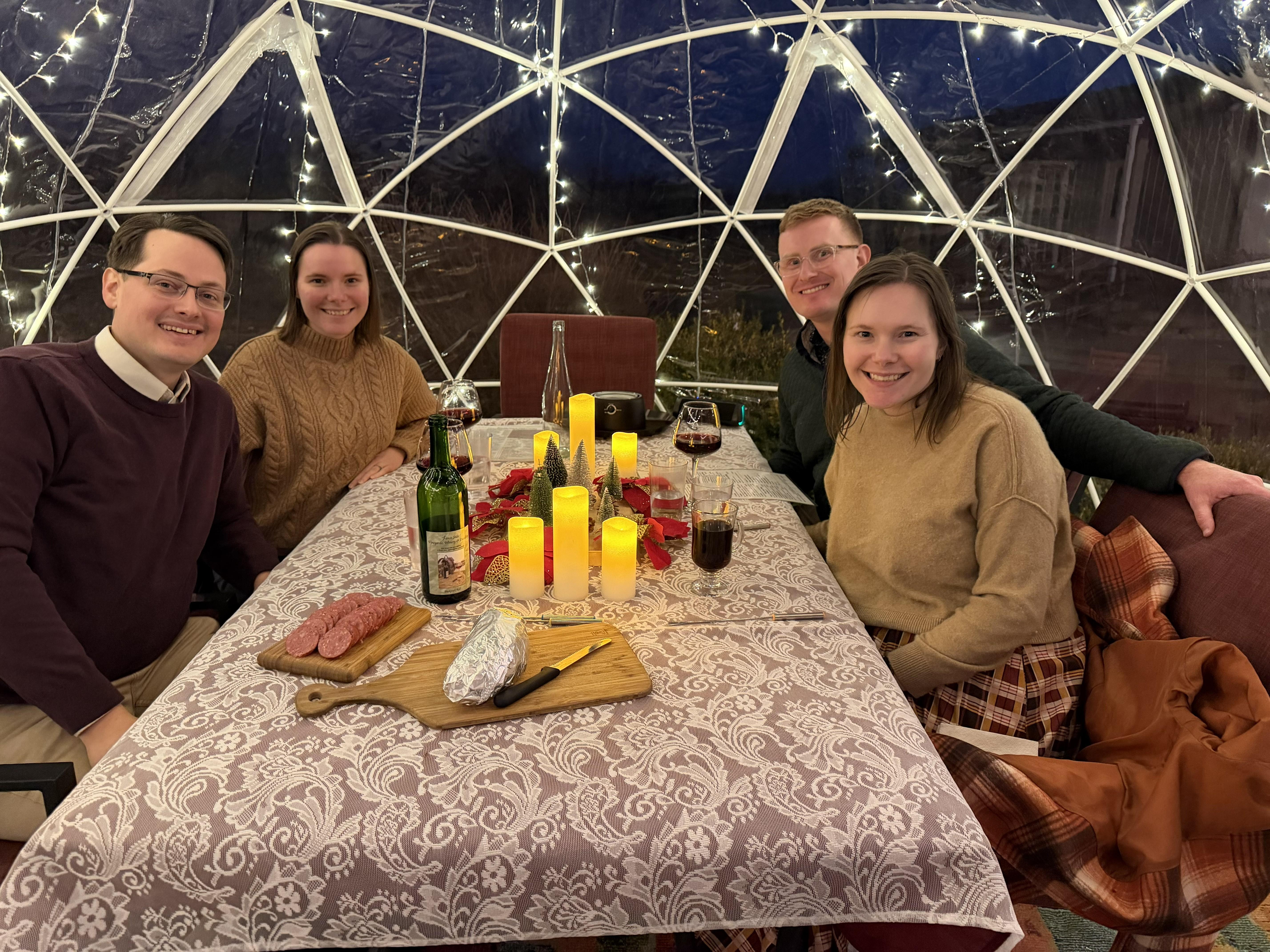 Four guests gathered around a warmly lit table inside a Fence Stile igloo at night
