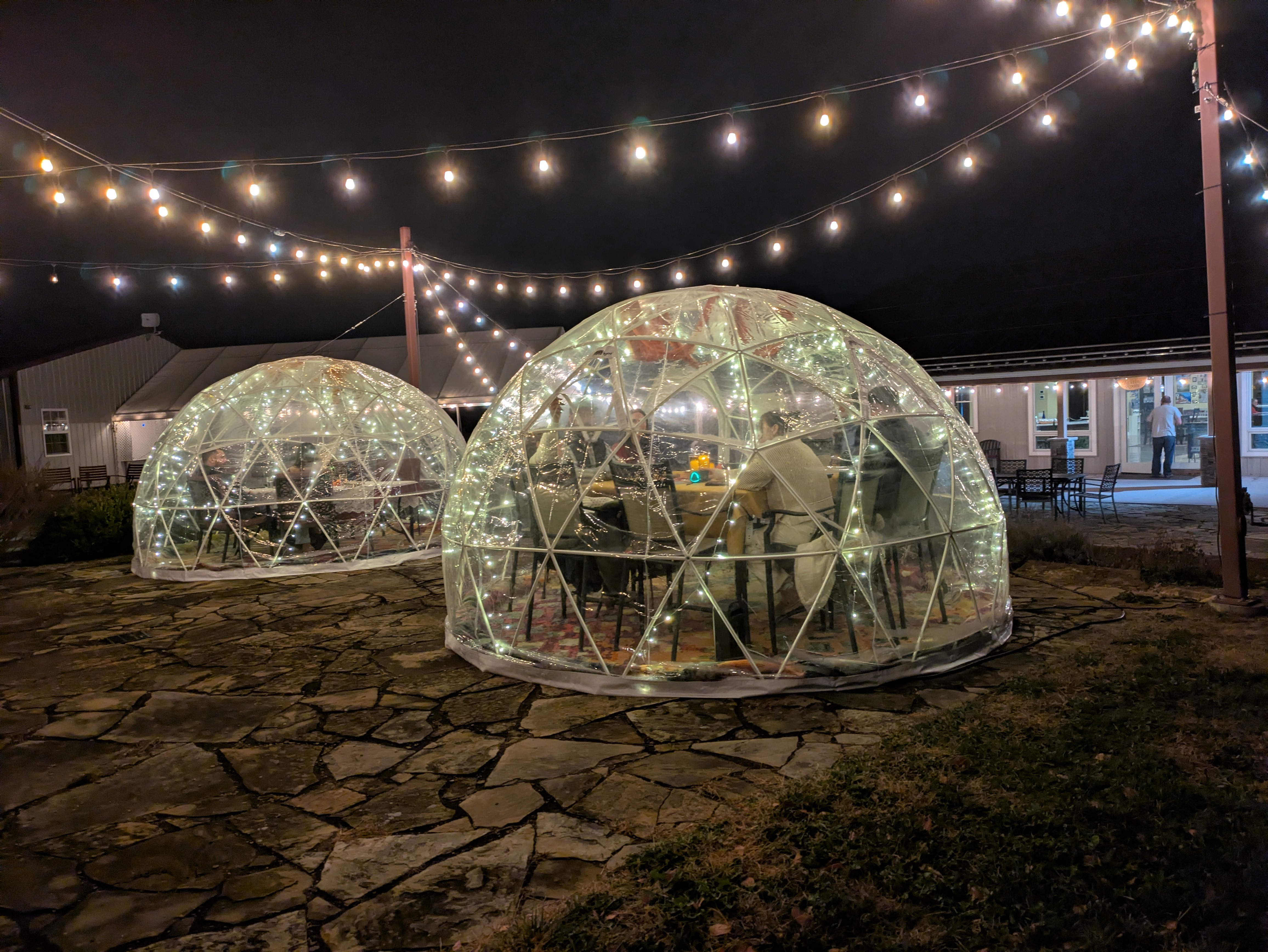 Two warmly lit Fence Stile igloos beneath the vineyard patio lights at night